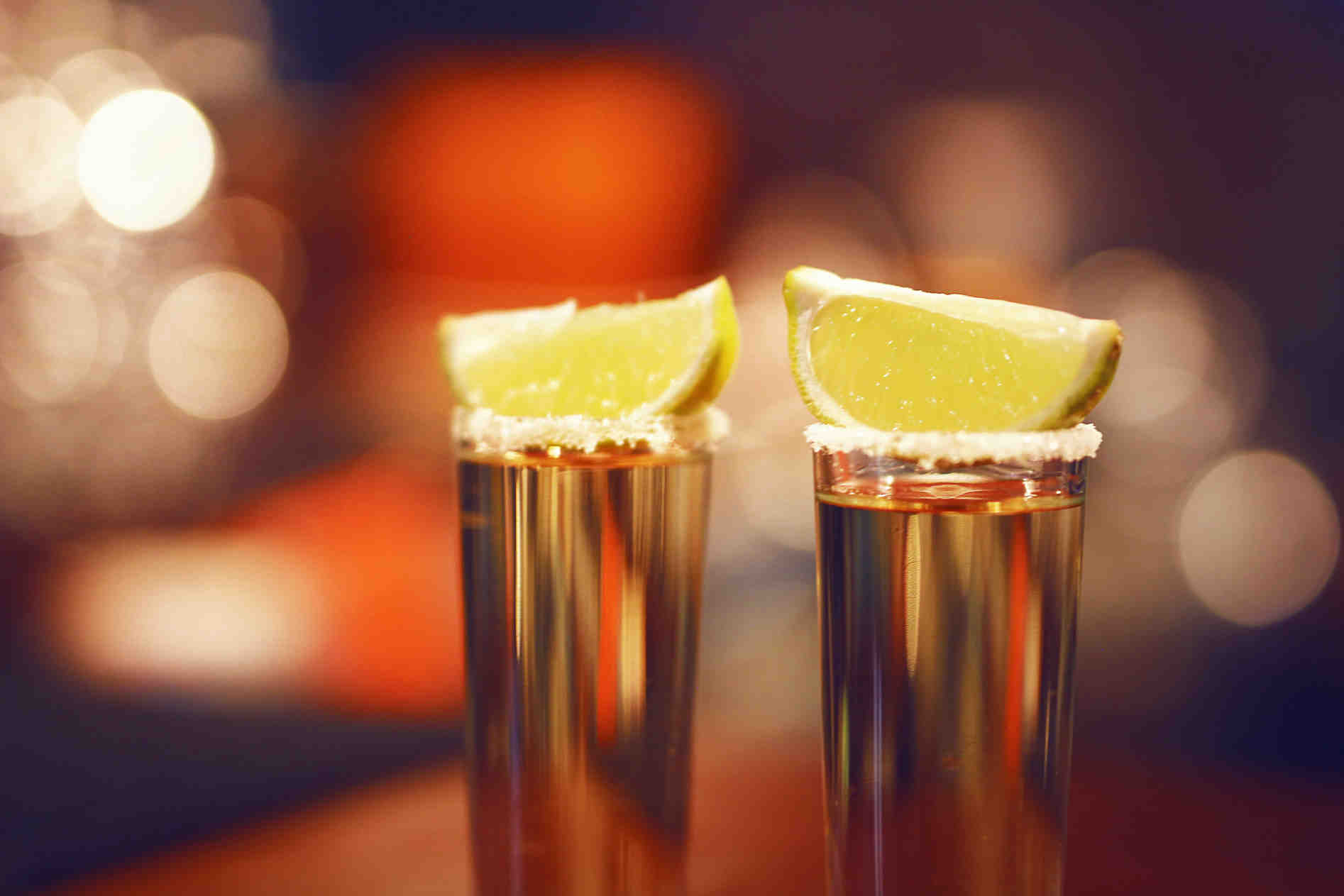Two glasses of extra añejo tequila topped with lime wedges and a salted rim, set against a warm, softly lit background.